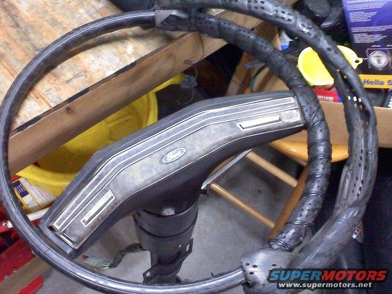 Ford steering wheel with a Ford logo on the center hub. The steering wheel is wrapped in black material
