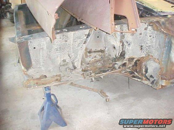 rusted car frame on blue jack stands, showing suspension components and body mounts
