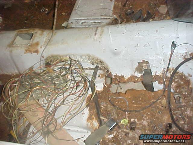 White car interior with a large bundle of tangled wires and rust damage