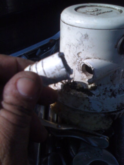 White plastic part with a broken pipe fitting held by a hand, showing grime and damage