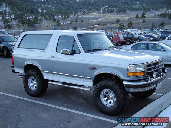 Silver and white Ford Bronco parked in a lot. It has aftermarket wheels and tires
