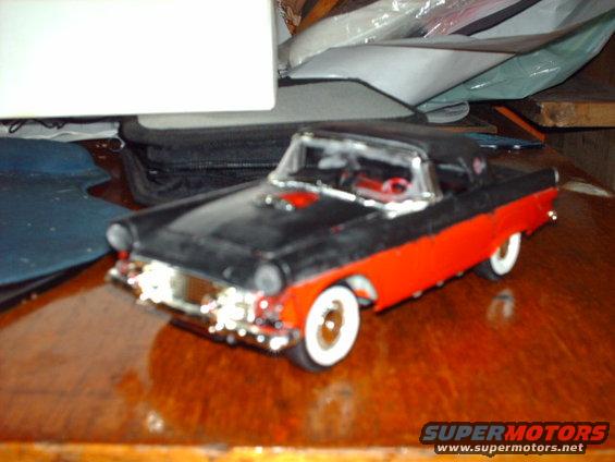 Black and red model car with chrome grille and whitewall tires on a wooden surface