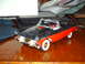 1978 Ford Mustang II - A two-tone model car sits on a reflective wooden table, with a white object and papers in the background.