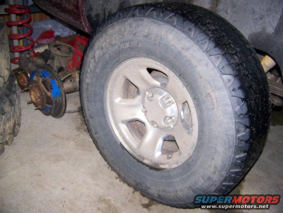 Close-up of a vehicle's wheel and some disassembled suspension components, including a red coil spring and brake parts