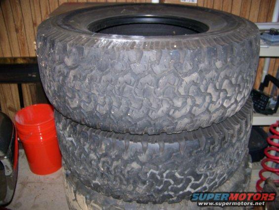 Stack of two used off-road tires, one on top of the other. A red bucket is to the left
