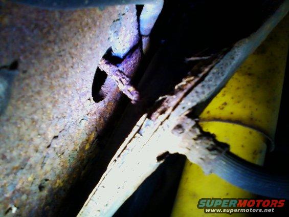 Close-up of heavily rusted metal frame with a yellow shock absorber and black hose