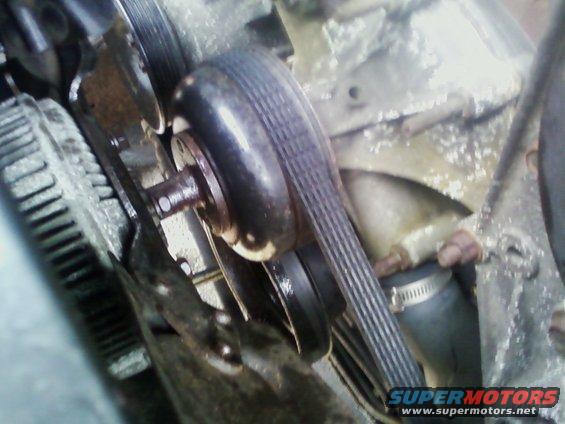Engine belt and pulley system with ribbed belt, pulley, and fan shroud. Water hose visible
