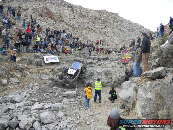 Off-road vehicle climbing a rocky hill with spectators watching. BFGoodrich banner visible