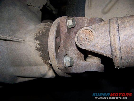 Close-up of a rusty driveshaft U-joint connected to a differential flange with bolts
