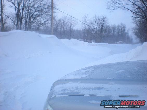 Silver vehicle hood covered in snow, driving through a snow-covered landscape
