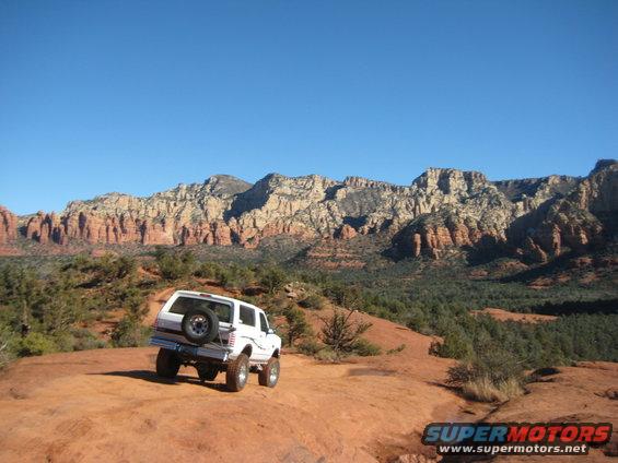 White 1996 Ford Bronco parked on a red rock trail with mountains in the background