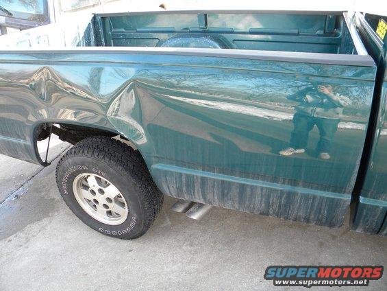 Side view of a green pickup truck with significant dents on the rear quarter panel and bed