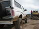 1996 Ford Bronco - A white Ford Bronco, caked in mud, is parked next to a trailer carrying a yellow Jeep in a dusty, outdoor setting.