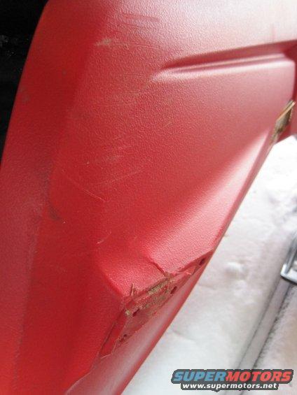 Close-up of a damaged red plastic panel, showing scratches and a cracked edge