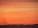 2006 Ford E350 - A vibrant sunset paints the sky with shades of orange and yellow, casting a silhouette over rolling hills and dry grass in the foreground.