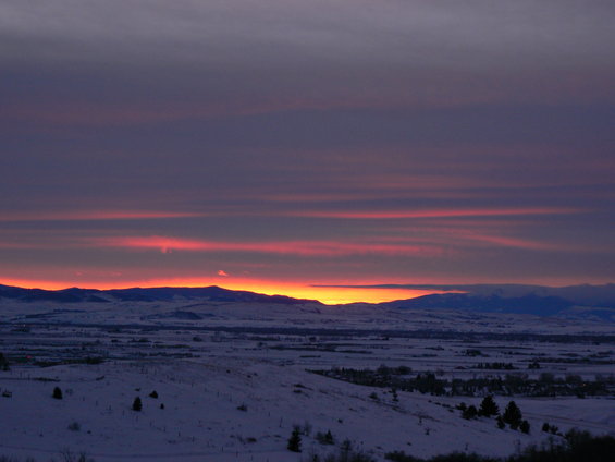 Snowy landscape with rolling hills and distant mountains under a colorful sunset sky