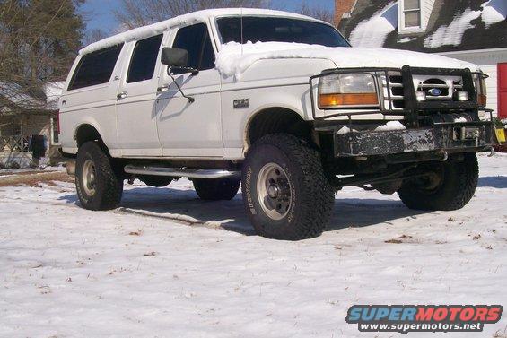 White SUV with snow on roof and hood, lifted with large tires, parked in a snowy yard
