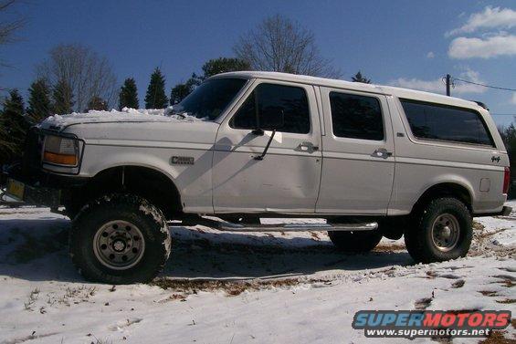 White 1992 Ford F-250 extended cab pickup with a camper shell, lifted with large tires, in a snowy outdoor setting