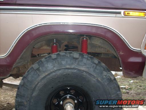 Close-up of a tan and maroon Ford Bronco's rear wheel well, showing a large tire and red shock absorber