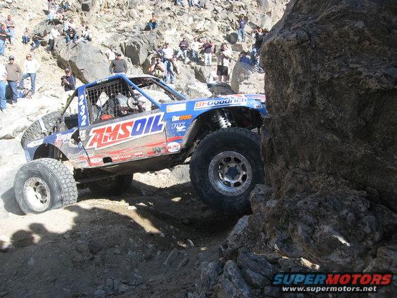 Blue off-road buggy with large tires navigating a rocky terrain, sponsored by AMSOIL and BFGoodrich