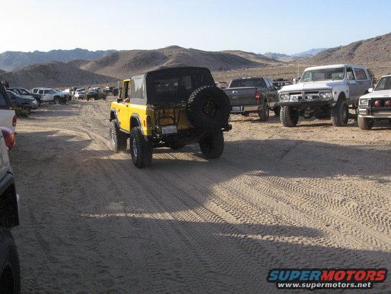 Yellow 1978 Ford Bronco with a soft top, spare tire, and aftermarket wheels parked on a dirt road