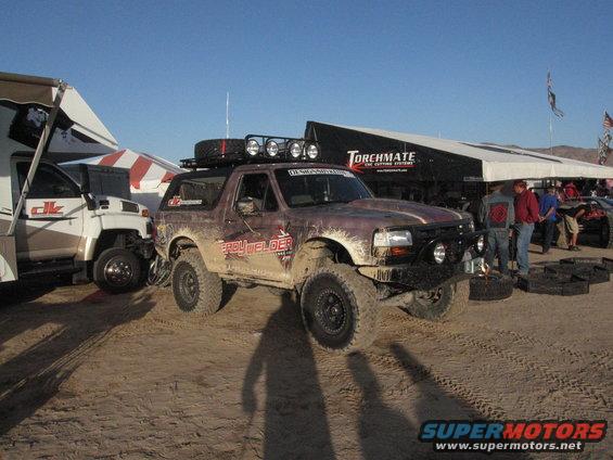 Brown Ford Bronco with roof rack and off-road tires, parked next to an RV