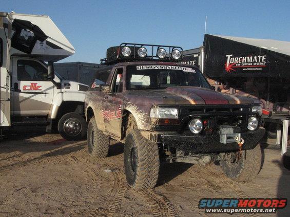 Mud-covered pickup truck with roof rack and winch, parked next to an RV