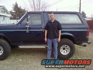 Guy standing next to a dark blue 1987 Ford Bronco