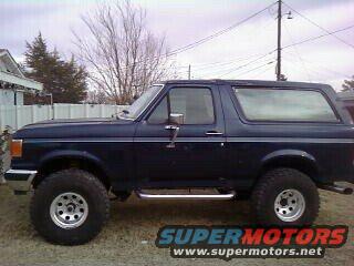Dark blue 1987 Ford Bronco with chrome side steps and large tires, seen from the side