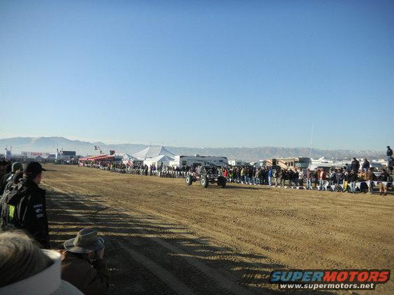 Off-road buggy driving on dirt track with spectators and tents in background