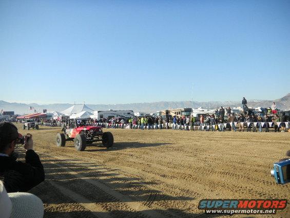 Red off-road buggy on sandy track with spectators and RVs in background