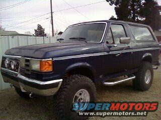 1987 Ford Bronco, dark blue, with aftermarket lights mounted on front bumper
