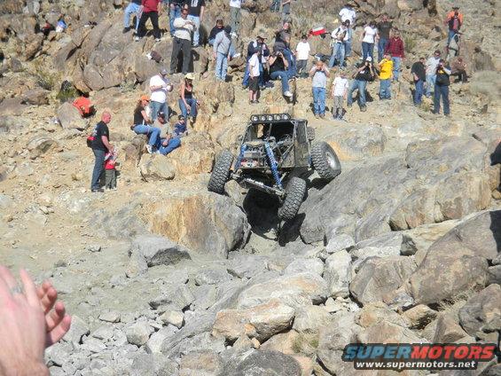 Off-road buggy climbing a rocky incline with spectators watching