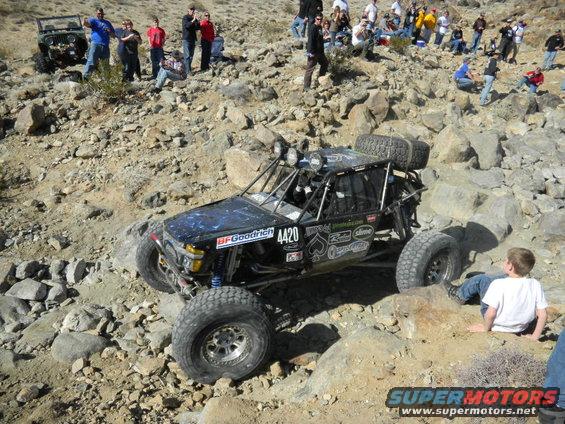 Black off-road buggy with large tires and a roll cage, navigating a rocky terrain