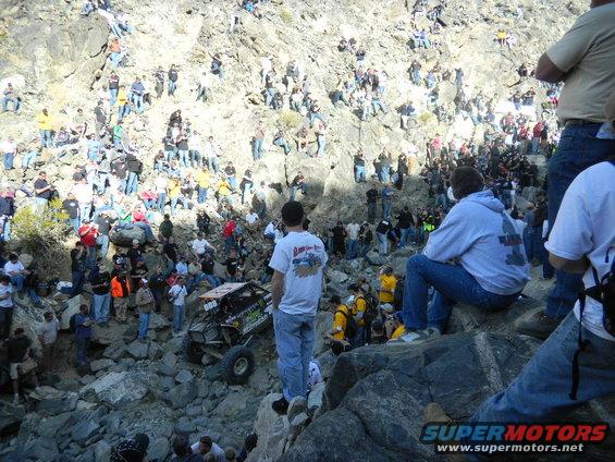 Off-road buggy with number 888 on side, climbing rocky slope with many spectators watching
