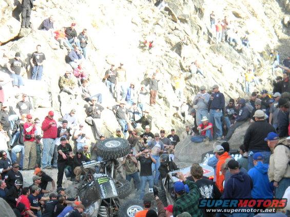 Off-road buggy overturned on rocky terrain with spectators watching