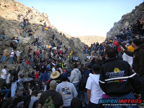 Crowd watches off-road vehicles navigate a rocky canyon during a race