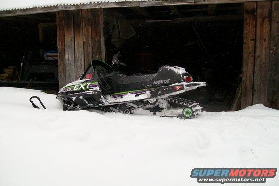 Snowmobile partially buried in snow outside a wooden structure