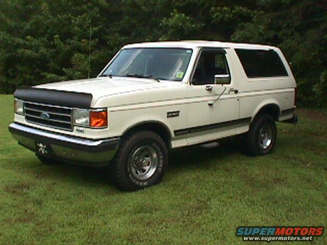 White 1990 Ford Bronco parked on grass with trees in background