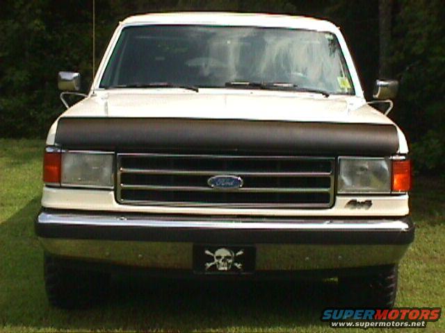 White 1990 Ford Bronco front view with a black hood protector and a skull and crossbones license plate frame