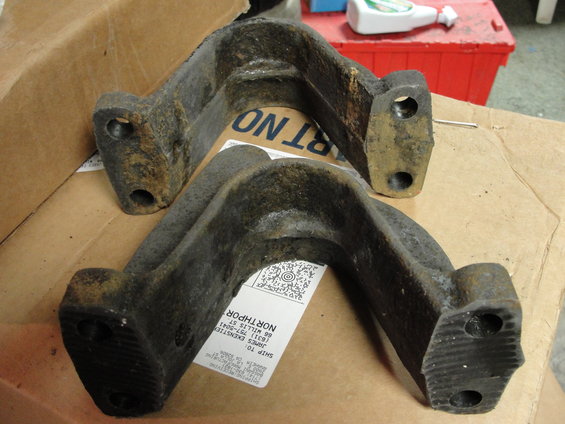 Two rusty, cast iron suspension parts sitting on a cardboard box