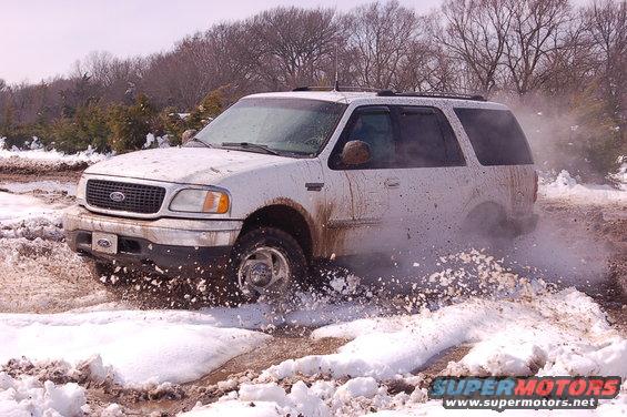 White 2002 Ford Expedition kicking up snow and mud while driving off-road
