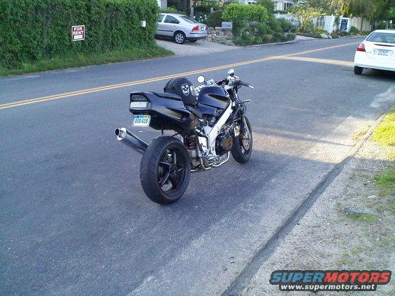 Black motorcycle parked on asphalt roadside, rear view. License plate reads 205-628