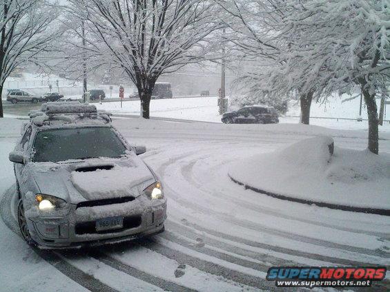 Silver Subaru Impreza WRX STI with roof rack covered in snow, driving on a snowy road