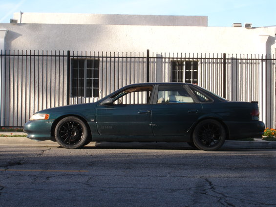 1995 Ford Taurus sedan, dark green, black wheels, parked on street