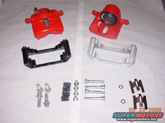 Two red brake calipers and assorted hardware laid out on a white surface