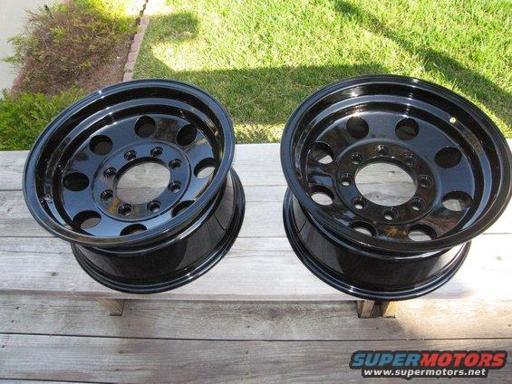 Two black steel wheels with multiple lug nut holes, resting on wooden planks