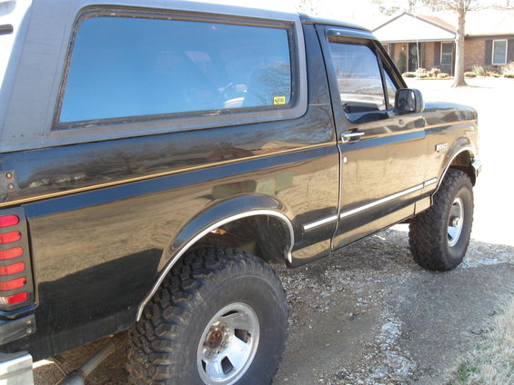 Black Ford Bronco parked on gravel, side view. It has a removable top and off-road tires