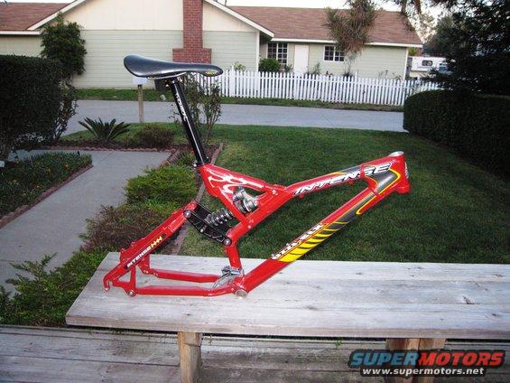 Red bicycle frame with black suspension and seat post, resting on a wooden bench