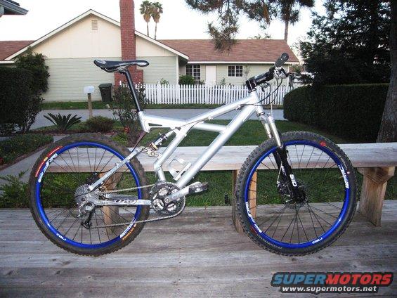 Silver full-suspension mountain bike with blue rims on a wooden deck